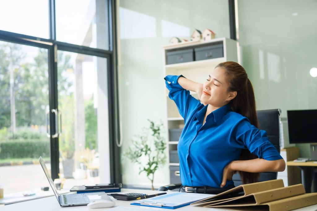 A businesswoman working at a desk in an office struggles with stress headaches caused by Office