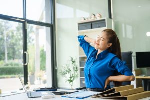 A businesswoman working at a desk in an office struggles with stress headaches caused by Office